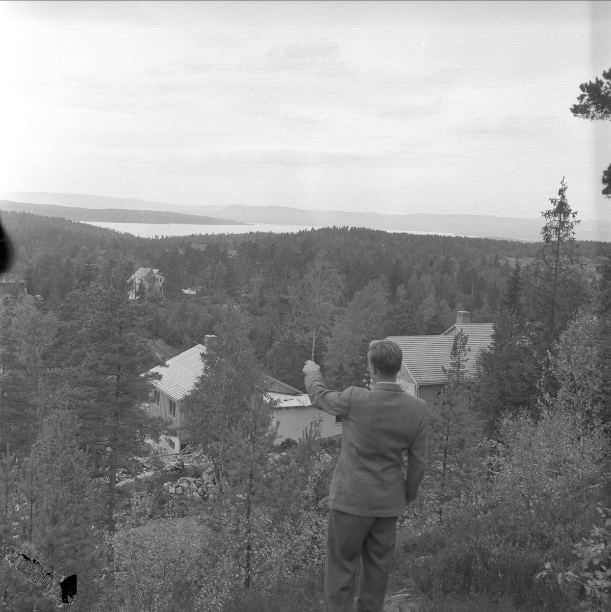 Søndre Oppegård, Akershus, 21.04.1956. Brukseier Eivind Sundt peker mot bygninger i skog.