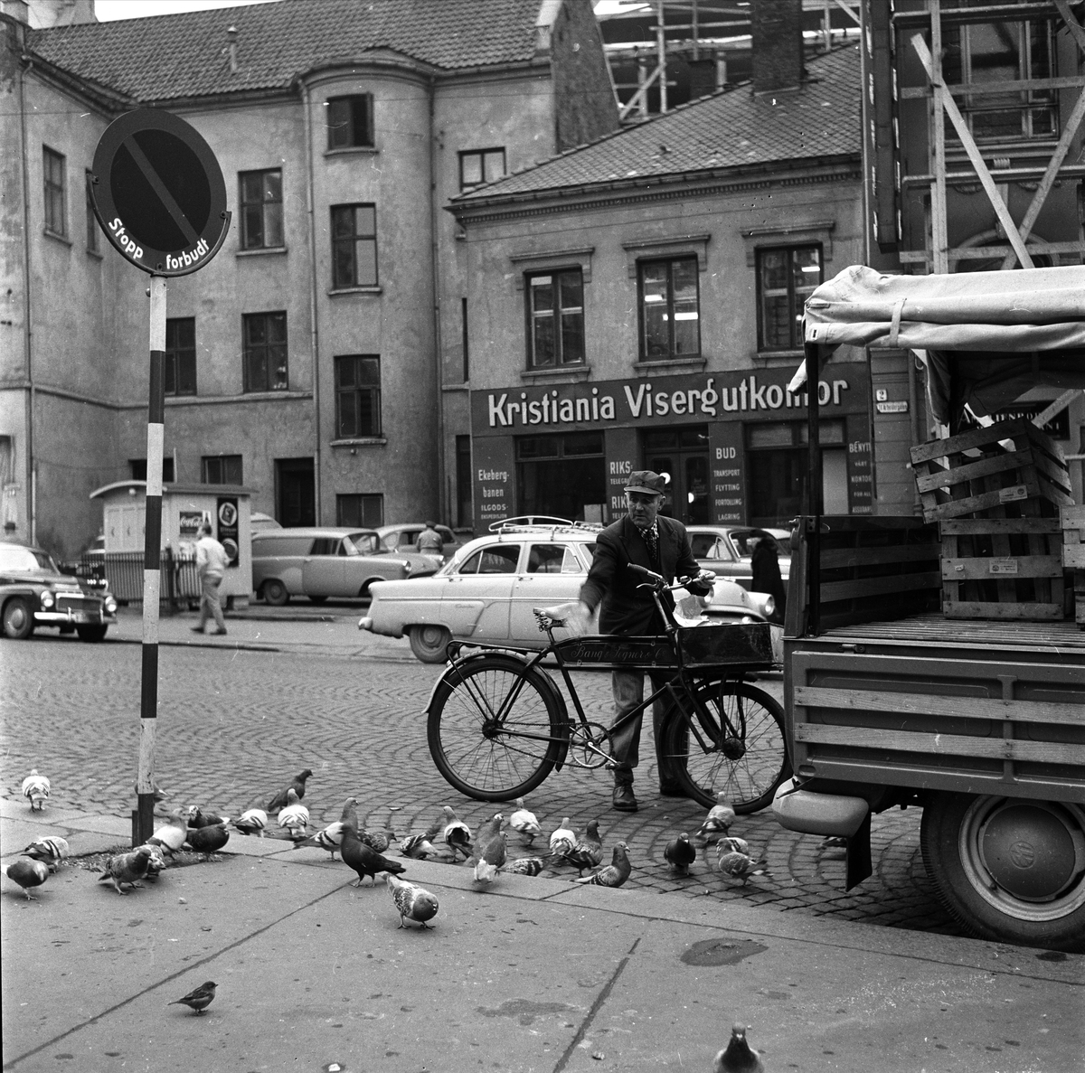 Professor Aschehougs plass, Oslo, oktober 1960. Bybilde med bygninger, biler og mann med sykkel.