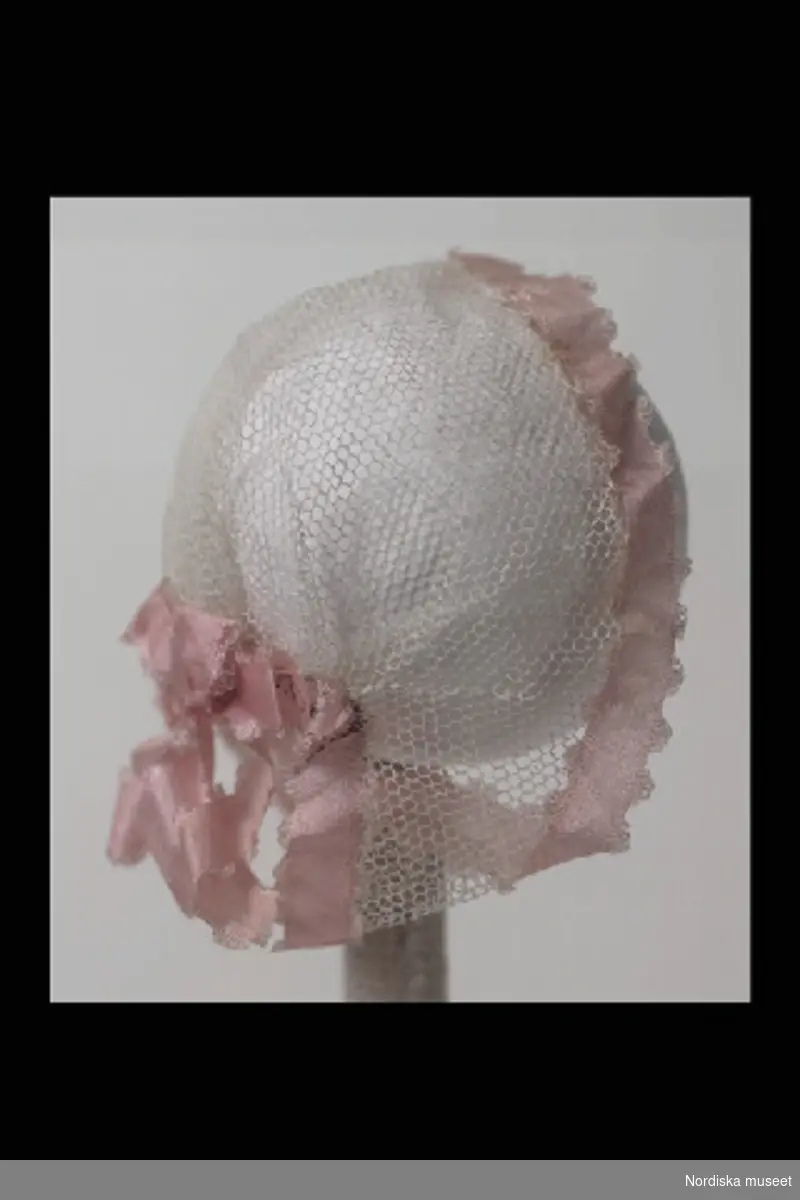 Inventering Sesam 1996-1999:
L 10 cm
Dockhårklädsel av vit tyll i form av hätta, kantad med rosa sidenband och rosett baktill.
Hör till docka inv.nr. 202.174
Leif Wallin jan 1997