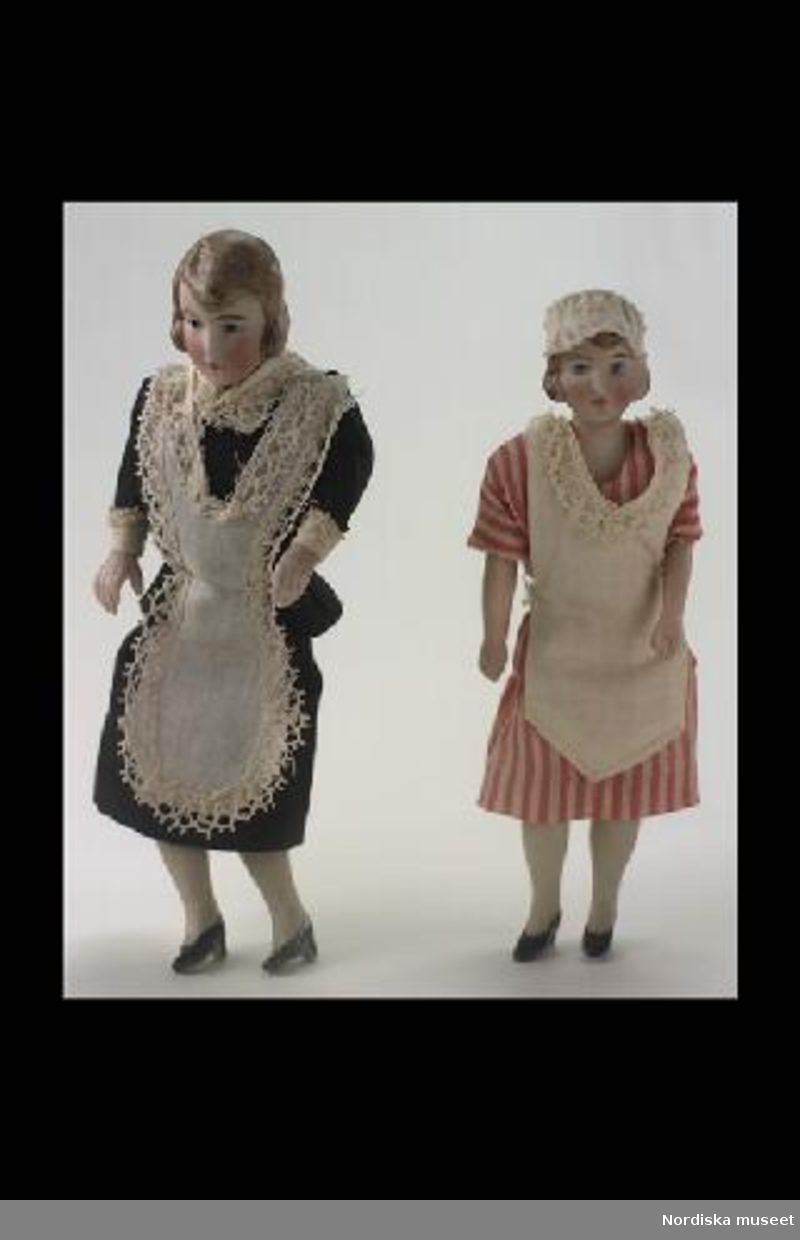 Inventering Sesam 1996-1999:
H 16 cm
Dockskåpsdocka föreställande husjungfru. Huvud med sköld, halvarmar och halvben av biskvi, målade anletsdrag, modelerat brunt hår (lös knut i nacken), stoppad kropp täckt med vitt tyg. Iklädd svart tvådelad klänning med vitt förkläde, vita mamelucker. Kläderna är fastsydda på dockan.
Brukad av Catarina (född 1919) och Anne-Sophie (född 1921) von Heidenstam, döttrar till givaren.
Tillhör dockskåp 220.405 med inv nr 220.406-220.760
Leif Wallin okt 1997