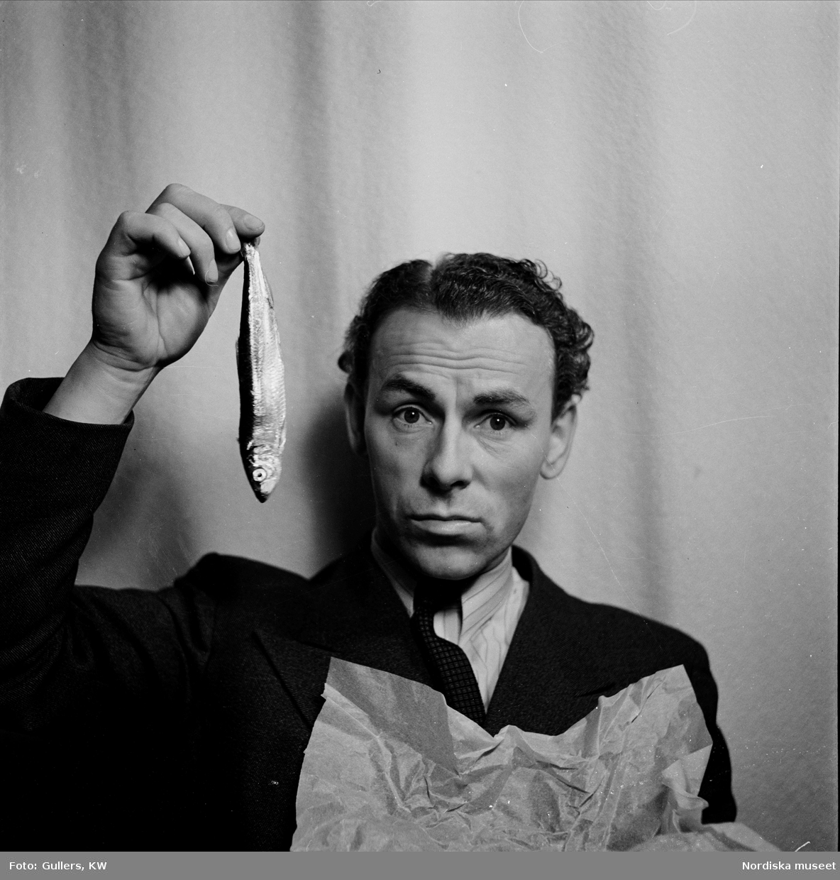 Nils Poppe (1908-2000), skådespelare och komiker, håller upp strömming med handen.