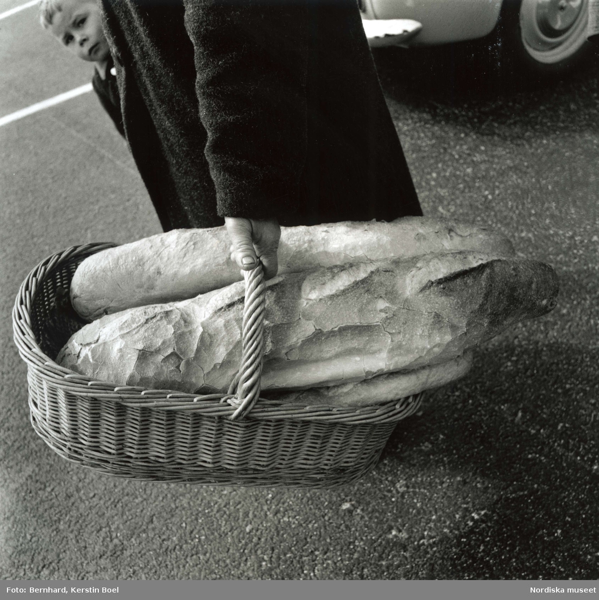 En kvinna bär två bröd i en korg. Bakom henne kikar en pojke fram.