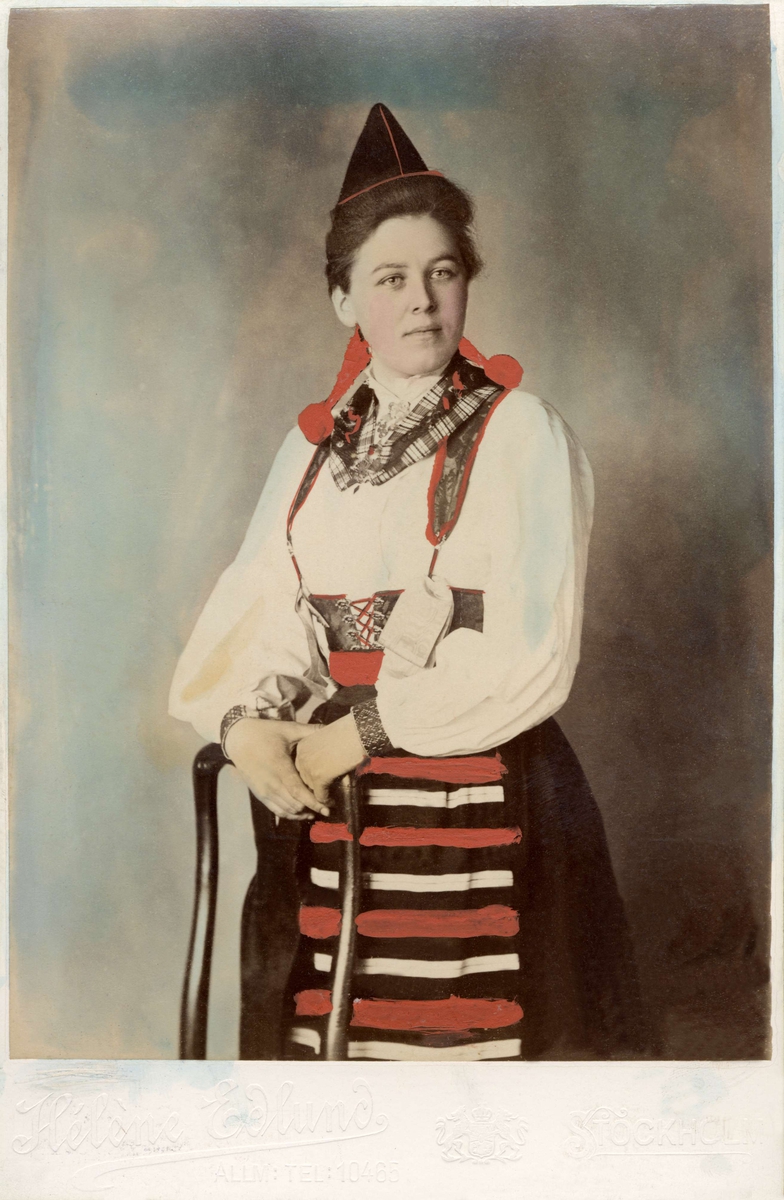 Kvinna poserar i en folkdräkt från Dalarna. Handkolorerat ateljéfoto.