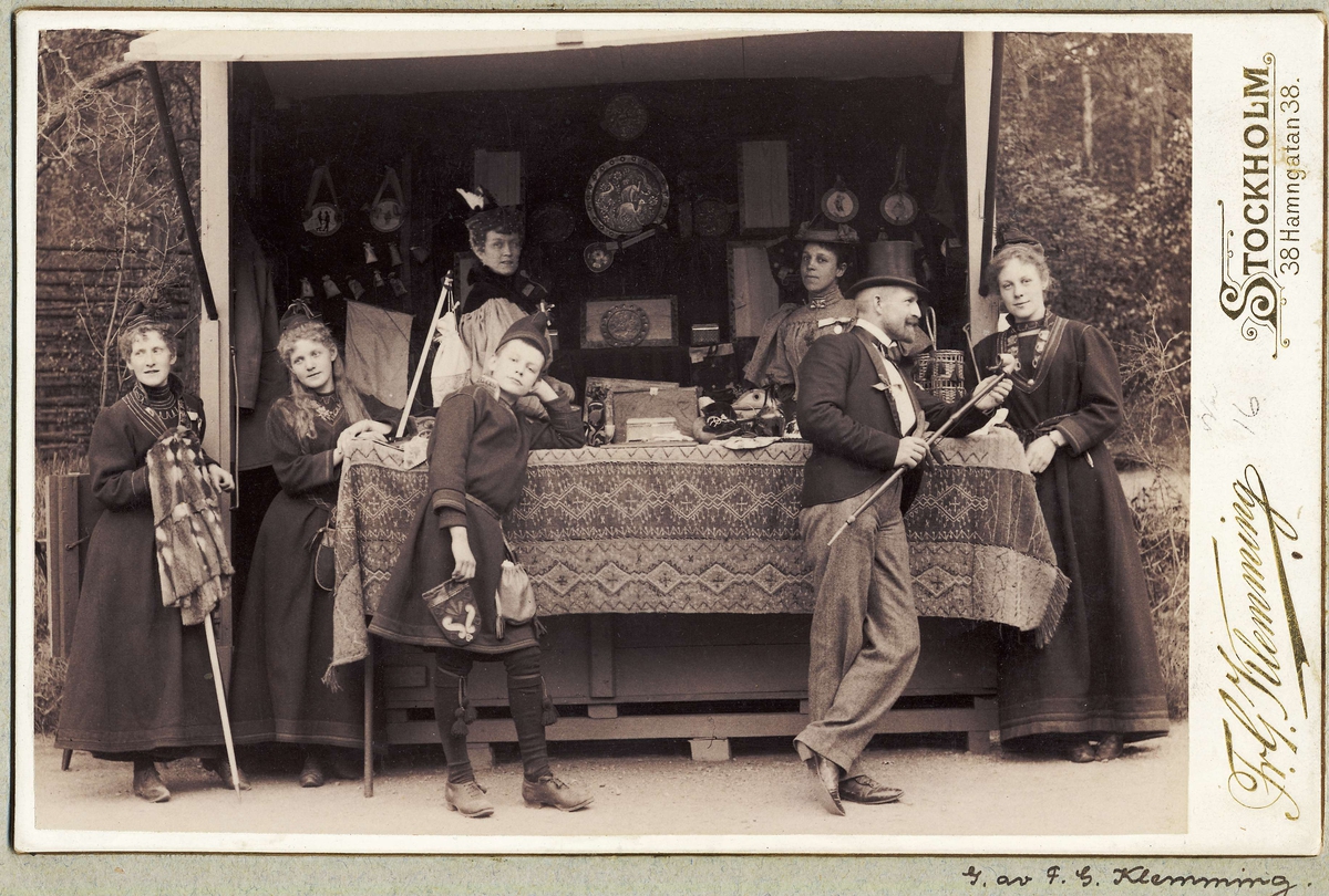 Skansens vårfest 1895. Herre i cylinderhatt och kavaj, kvinnor och pojke i samiska kläder vid bod med samehantverk