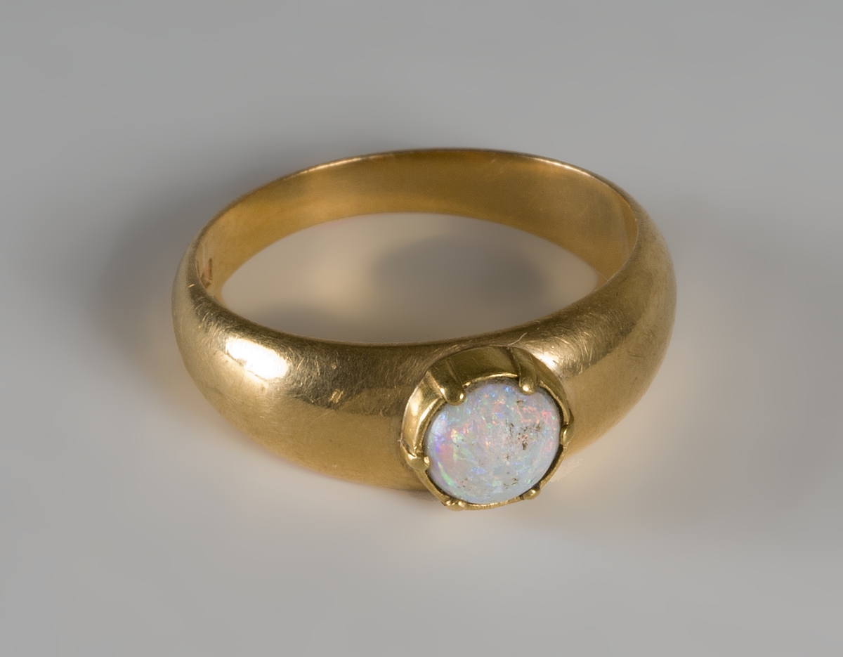 Guldring med ljusblå opal. Stämplar: MWR, U, tre kronor, 18 K, X5.

