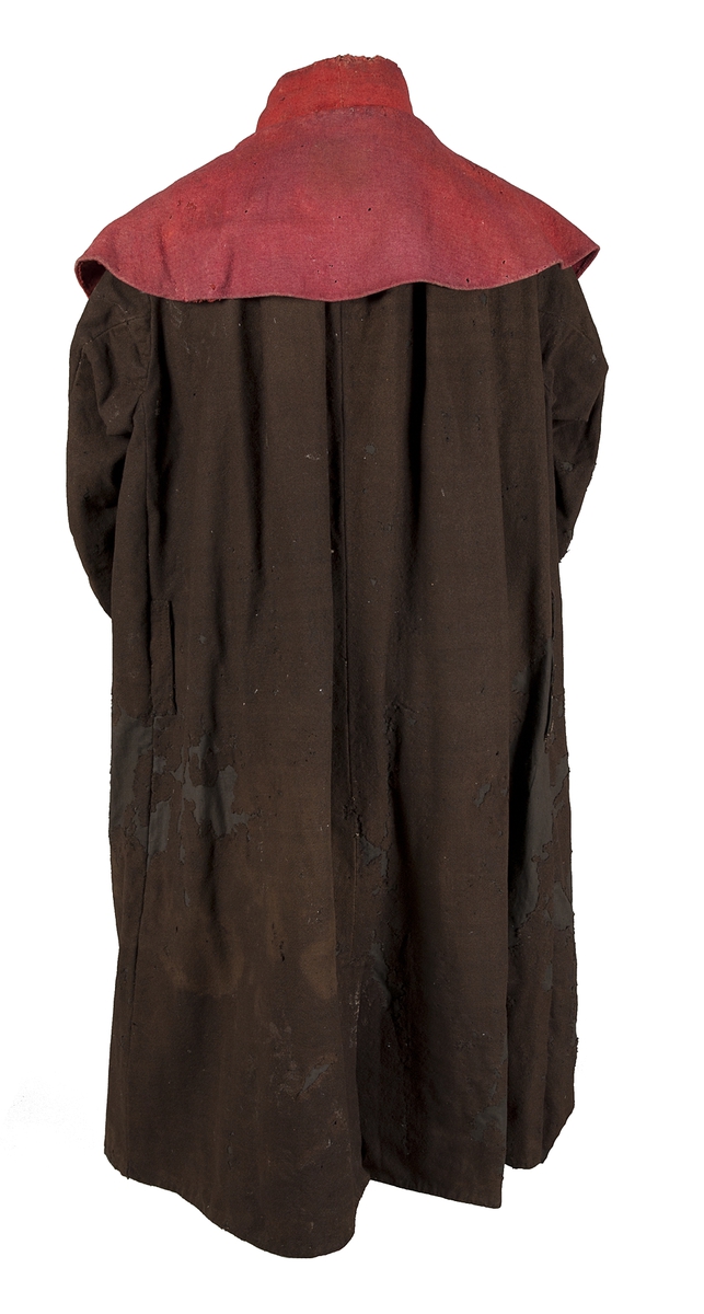 Kyrkvaktarrock av brunt grovt kläde med röd krage och ärmuppslag av vadmal. Tre knapphål sydda med svart tråd. Sprund bak.