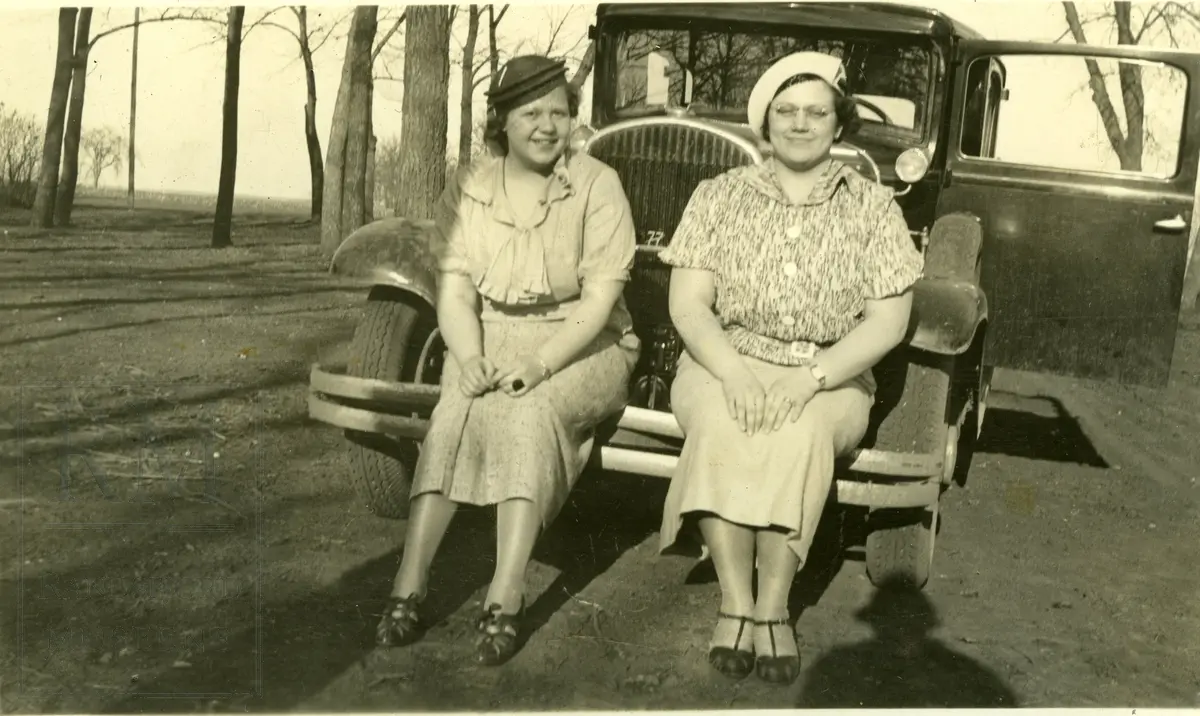 To kvinner sittende på støtfangeren til en bil.