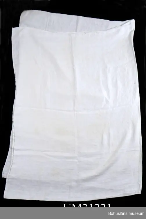 Mindre, kvadratisk handduk av vit frotté.  Mindre, rektangulär invävd relieftext VARMBADHUSET 
i kortändarna. Dessa handdukar har kanske använts som sitthandduk i bastun (?)  
Slitna kanter, några gula fläckar.