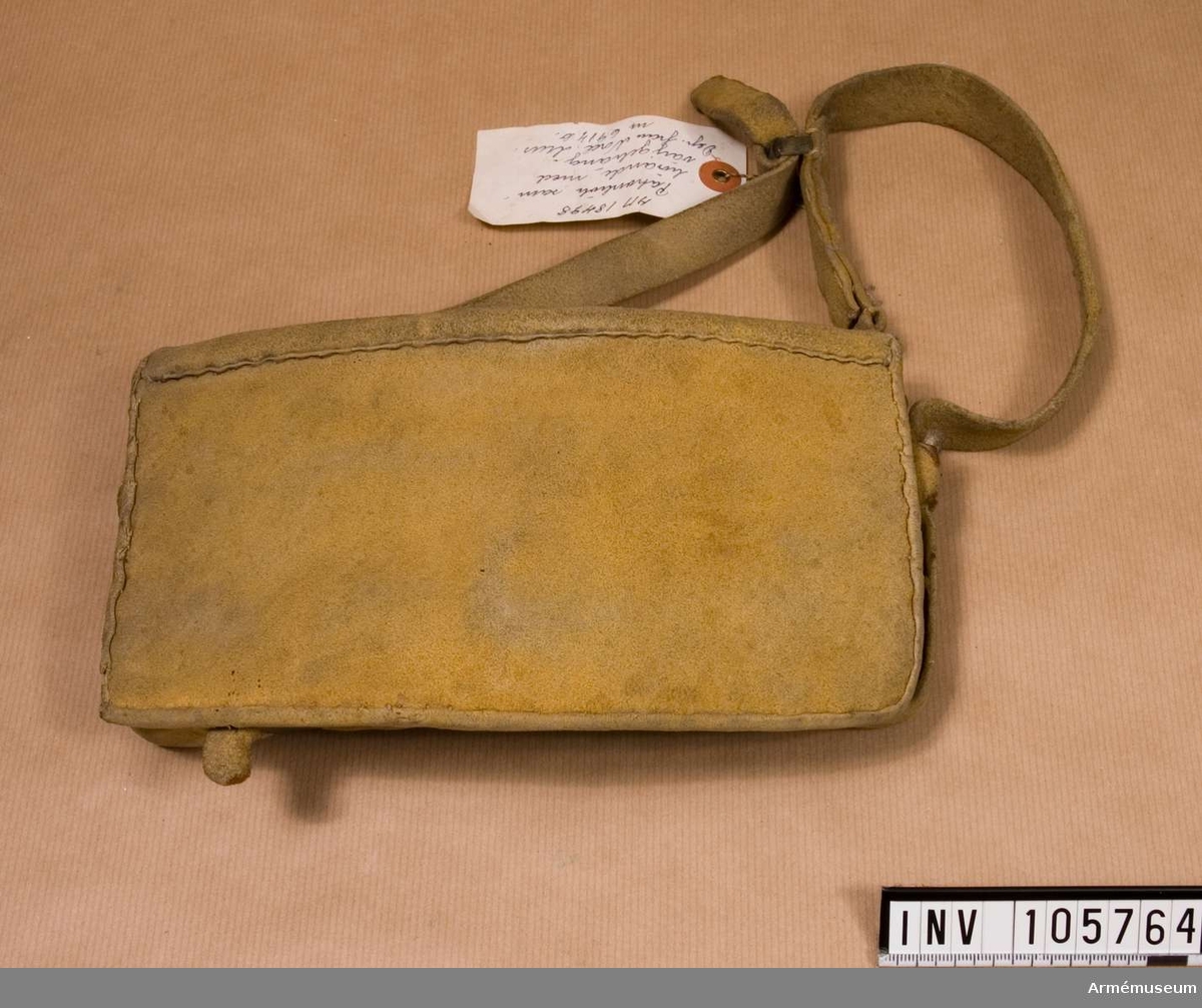 Patronväska av gult sämskat läder, med rem.
Inuti kartuschen sitter en bleckplåtsinsats med rum för 11 patroner av 18 mm kaliber.