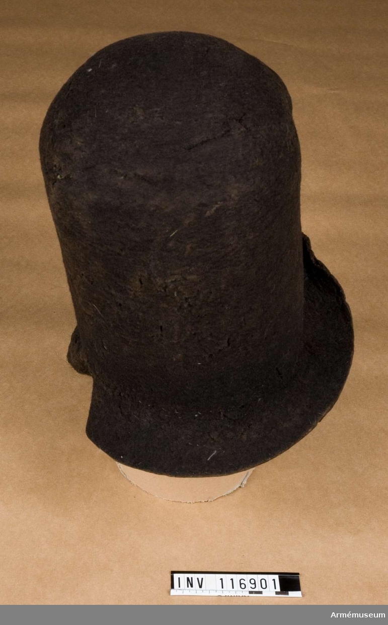 Hatt av svart filt med mässingskordong och vit pompong.