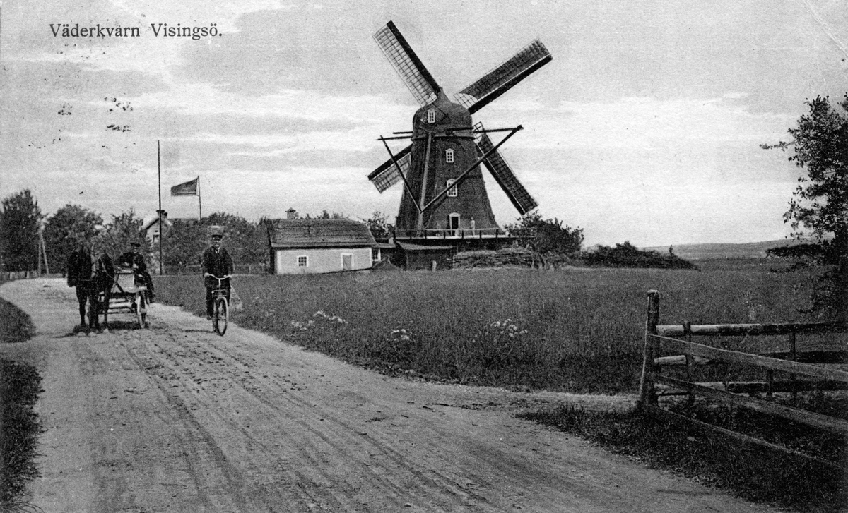 En väderkvarn på Visingsö. På grusvägen cyklar en man och en annan färdas med häst och kärra. Vykort skrivet 1923-07-22.