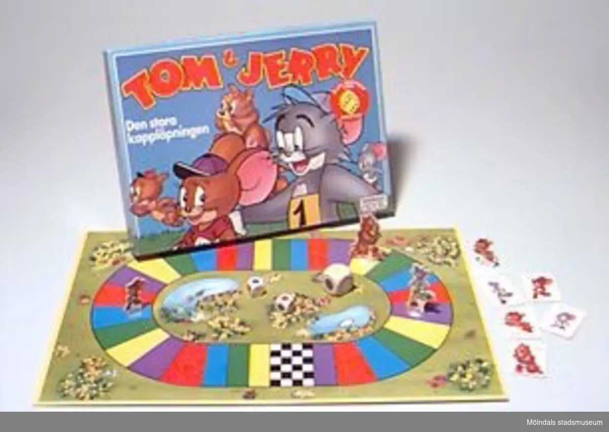 Sällskapsspel för barn. Ett sk färgtärningsspel. Spelet heter Tom & Jerry - den stora kapplöpningen. För barn över 4 år, 2 - 5 deltagare. Kartongen innehåller: en spelplan, 5 spelfigurer med hållare, 5 stycken bildkort, 3 färgtärningar och spelregler. Spelet fick utmärkelsen "Årets barnspel 1992", enligt annonsen på spelkartongens ovansida. Givaren är Katrinebergs daghem.