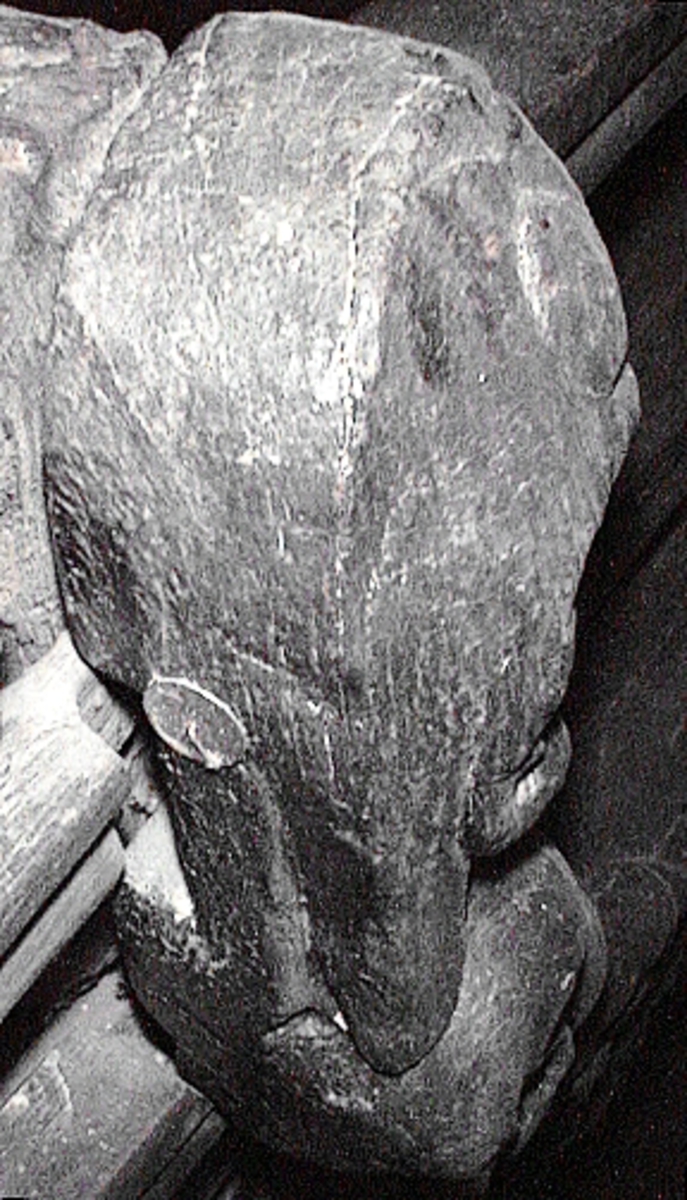 Skulptur föreställande en triton, svängd mot vänster och framställd i höger profil.
Tritonen har skäggigt ansikte, stor näsa samt en bladsmyckad hjälm på huvudet. Armarna är ersatta av långa, flikiga bladslingor. Bålens övergång i den fjällförsedda fiskstjärten markeras av stora bladbildningar. Figuren avtecknar sig i hög relief mot det släta bakstycket. Nedtill ses en fiskliknande stjärt med drakfena, vilken är fortsättningen på en under liggande draken, se fyndnummer 00628. På baksidan finns urtag för relingslisten.
Skulpturen är välbevarad.

Text in English: A sculpture of a Triton curved to the left, in right profile.
Bearded face with a long nose. Leaf-decorated helmet. The arms are replaced by long, lobed leaf formations. The transition between the male torso and the scaled fish-tail is decorated with large leaves. The figure is seen in high relief against a plain back board. Below the figure can be seen a section of another fish-like tail but actually a dragon''s fin, belonging to the dragon situated underneath, see No. 00628. There are notches on the back of the sculpture that fit into the railing.
The sculpture is well preserved.