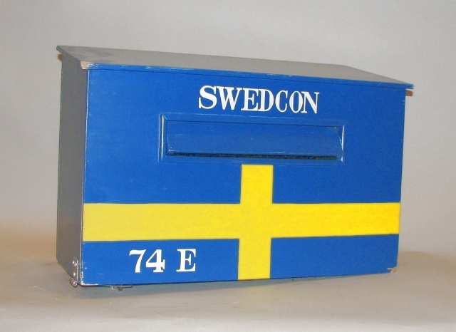 Brevlåda i trä med klaff för iläggsöppningen.
Iläggsöppningenhar mått:L=330 mm, H=40 mm. På fronten är lådan målad som den svenskaflaggan. Tömningslucka i botten, låsbar med hänglås.