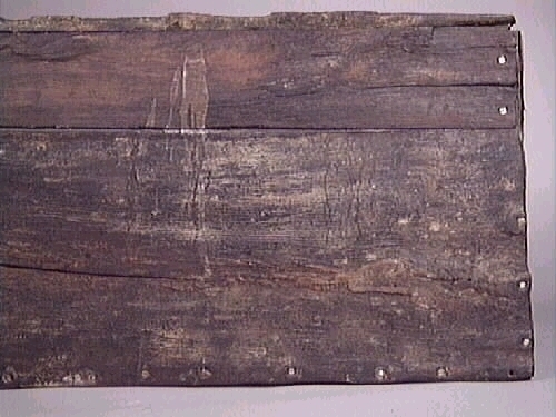 Del av baksida till en kista (botten del). Trästycket är brutet och i relativt dåligt skick.