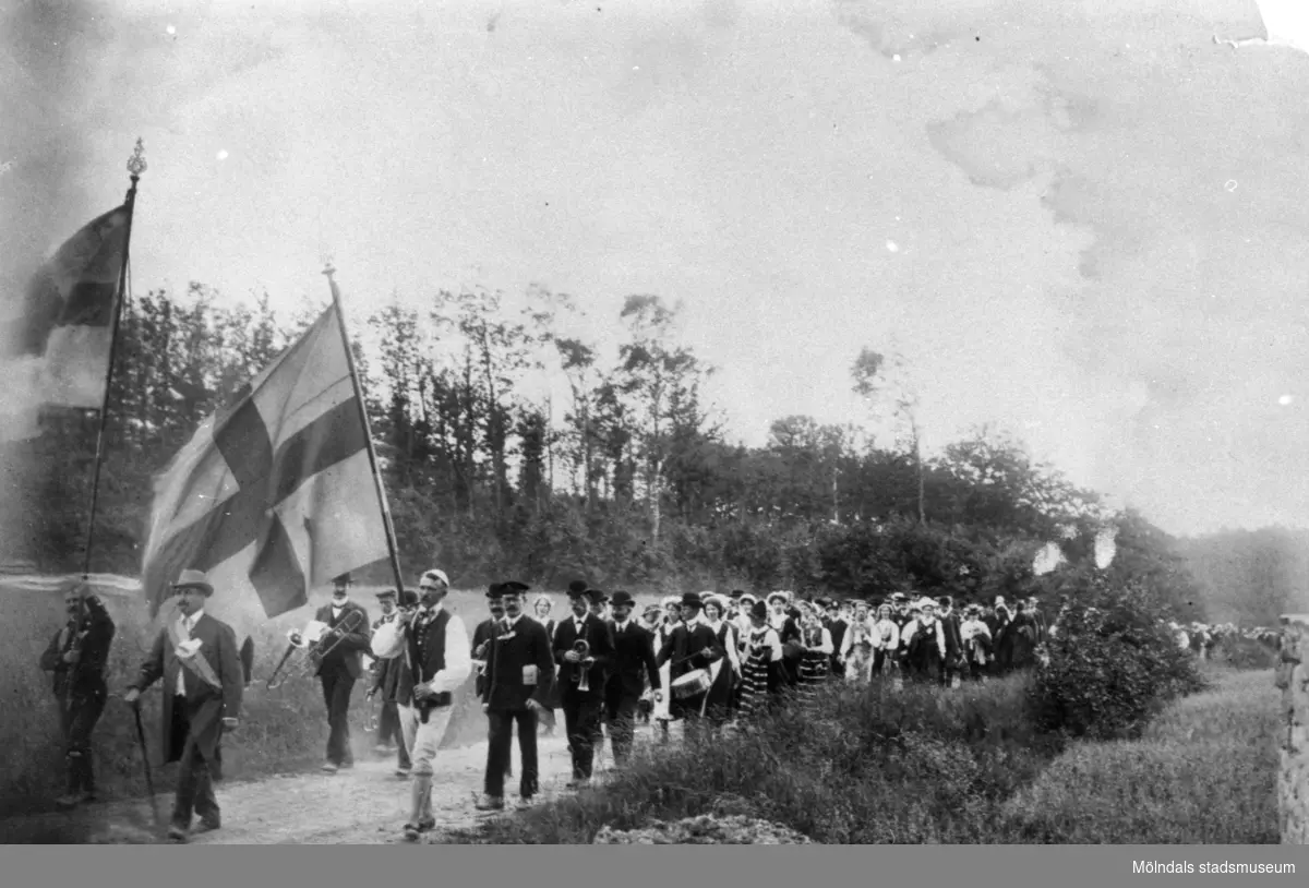 Festtåg med flaggor och musikkår vid Råda kyrka i samband med en sommarfest. I spetsen går ingenjör Falgren. Okänt årtal.