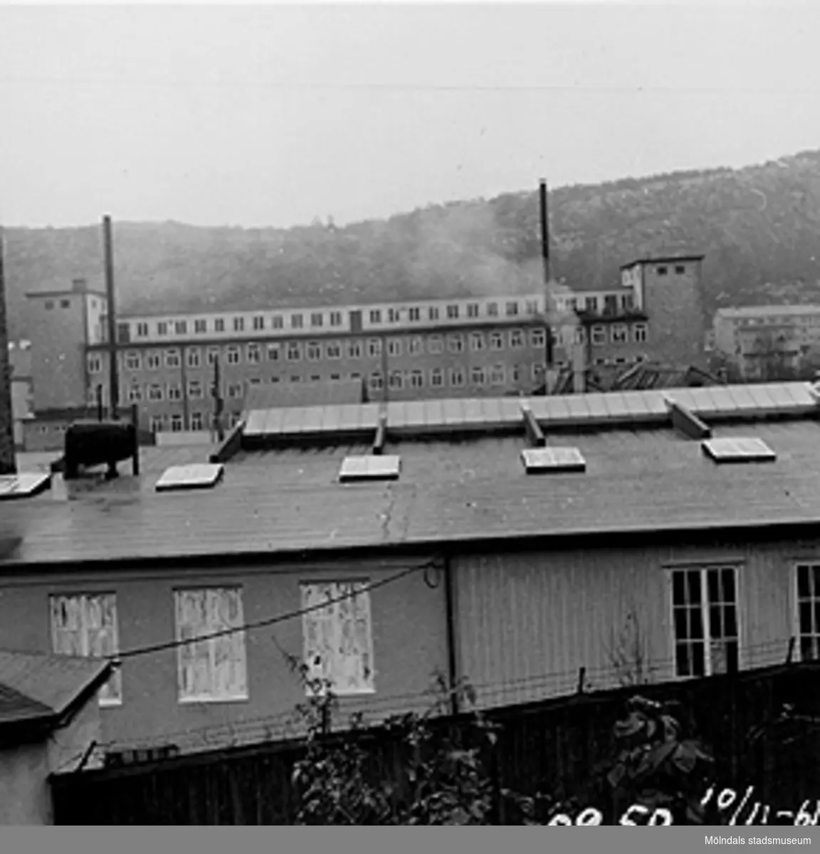 I förgrunden ses takåsarna på en fabriks- och verkstadsbyggnad (Åbäcksgatan 8), 1961. Bakom dessa ligger Lindenhofs höga byggnad på Åbäcksgatan 6A. Enligt vad Krokslättsborna berättar uppfördes huset på 1950-talet. I bakgrunden ses Rallarberget där Siemens fabriksbyggnad skymtas till höger.