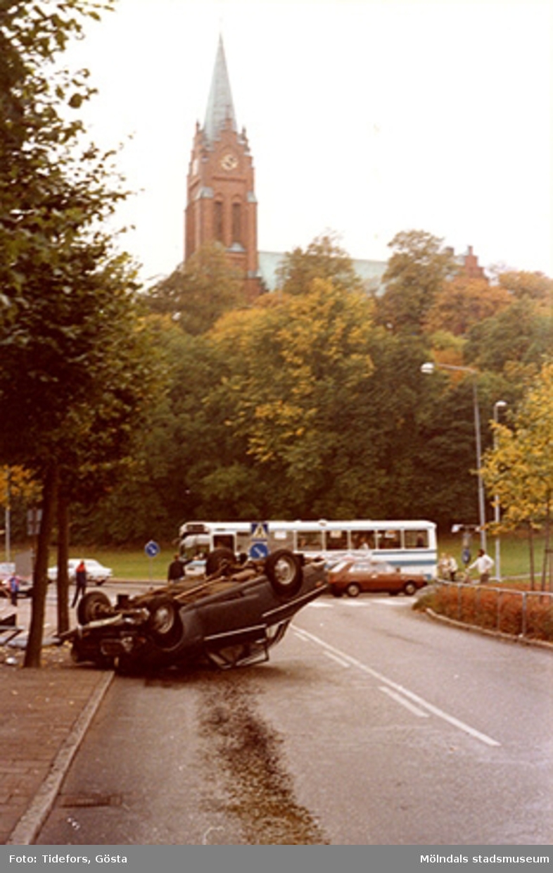 Olyckan har skett innan korsningen Häradsgatan och Tempelgatan mot Fässbergs kyrka, 1970-tal. I bakgrunden ses en buss samt människor som väntar vid övergångsställe.
