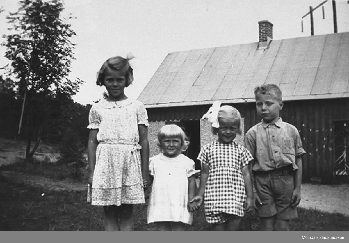 Sommar i Lindome, början av 1940-talet. Fyra barn poserar framför kameran. I bakgrunden ses en lada.