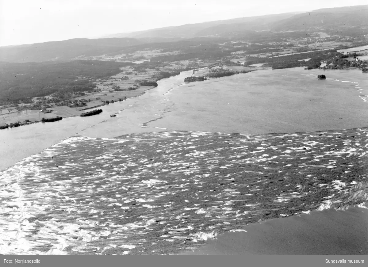 Flygfoton över Marmen som är fylld av timmer på väg ned mot kusten. På en av bilderna syns Attmars kyrka till vänster och Tuna kyrka till höger.