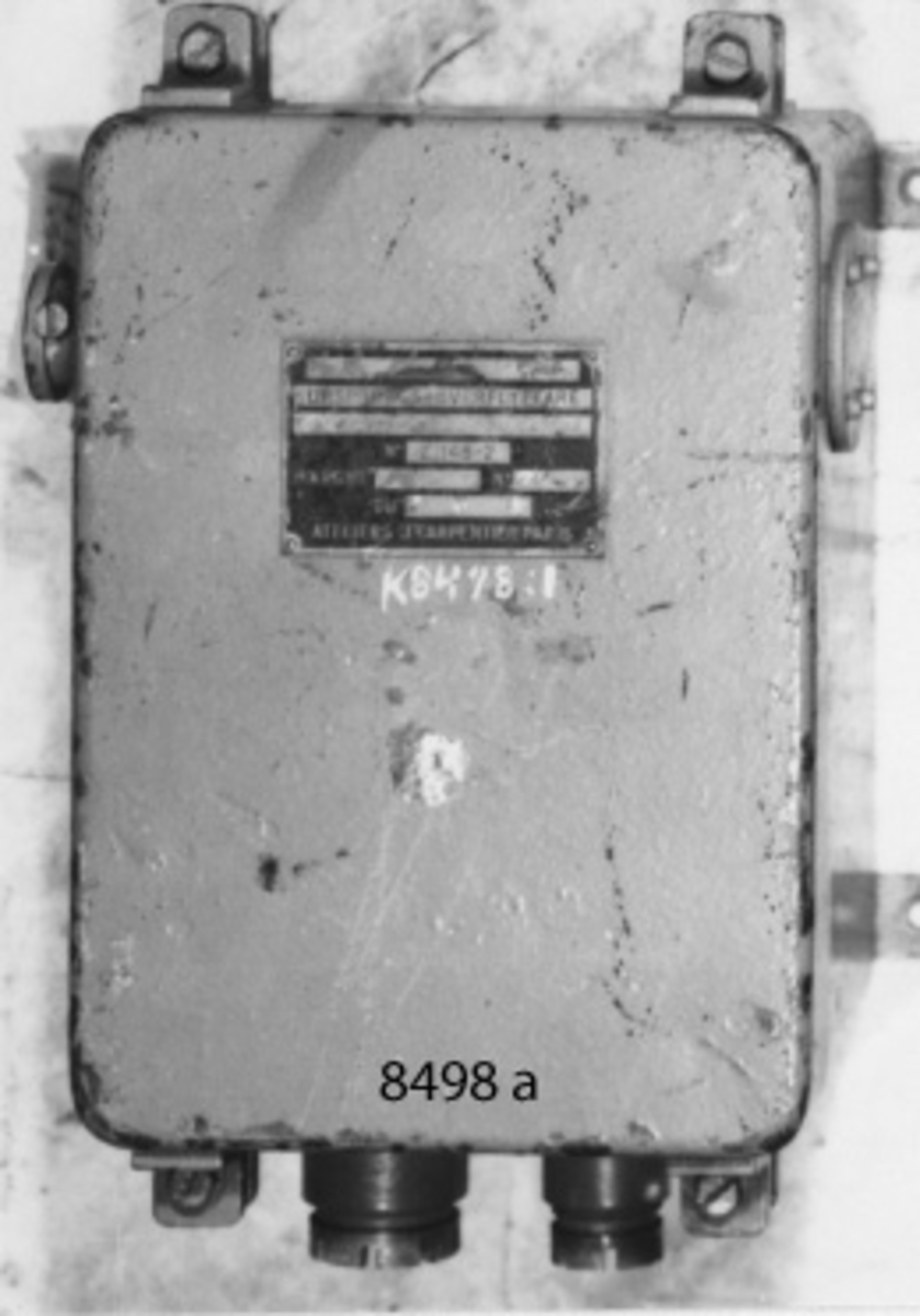 Ursprungsöverflyttare (avgivare) i en låda av gjutjärn med lock, som fasthålles av fyra skruvar. På undersidan två kabelintag, på vänster sida en genomgående rörlig axel med kopplingshylsa. Gråblå. Märkning: Ursprungs-överflyttare No Z 148-2 Ateliers J Capertier Paris