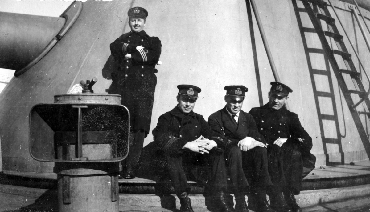Fartygbefäl i uniform poserar vid kanon. Tre sitter och en står med armarna i kors på kanondäck.