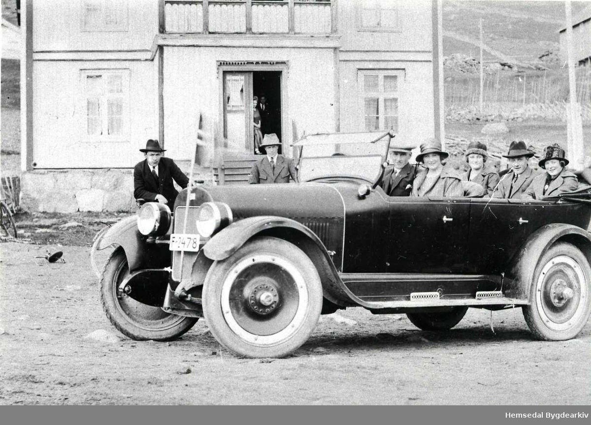 Frå venstre: Jon Hjelmen, Halvor K. Mythe, båe frå Hemsedal,  og sjåfør Knut Granheim frå Gol. Dei andre er ukjende. Bilen er ein 1923 Buick.