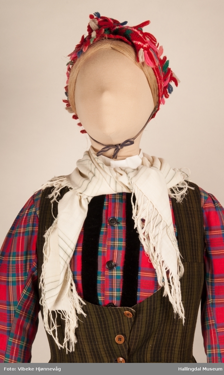 Kone fra Hemsedal i heljestakk fra Hemsedal. Kona står utstilt i den faste bunadutstillingen på Hallingdal Museum, Nesbyen.  Bunaden består av mange draktdeler; trøye, stakk, skjorte, hodeplagg, lue og skaut rundt halsen.