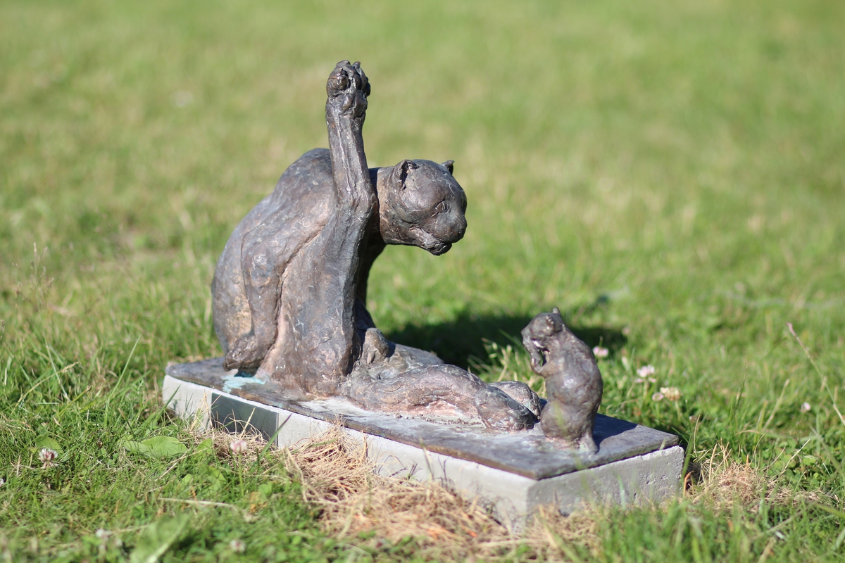 Skulptur i bronse av en katt som vasker seg. Tittel: "Pus vasker seg og mus ser på"
