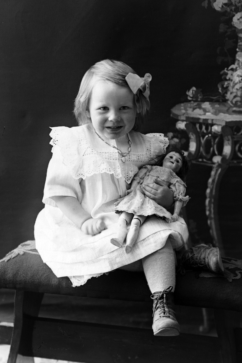 Studioportrett av en liten jente med dukke på fanget.