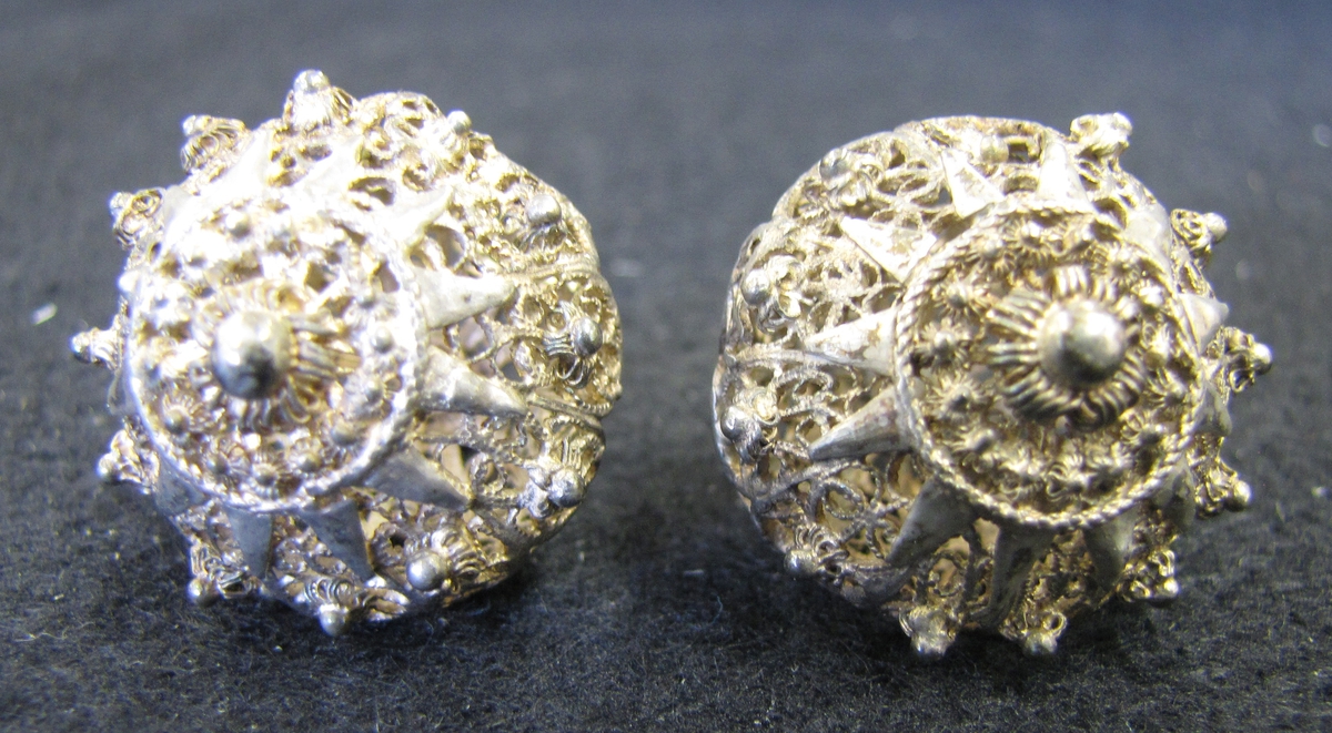 Två runda silverknappar med ögla. Knapparna är uppbyggda av genombruten filigran. Enligt Vänersborgs museums katalog av år 1905 härrör knapparna från Norge, en uppgift som ej kunnat styrkas.