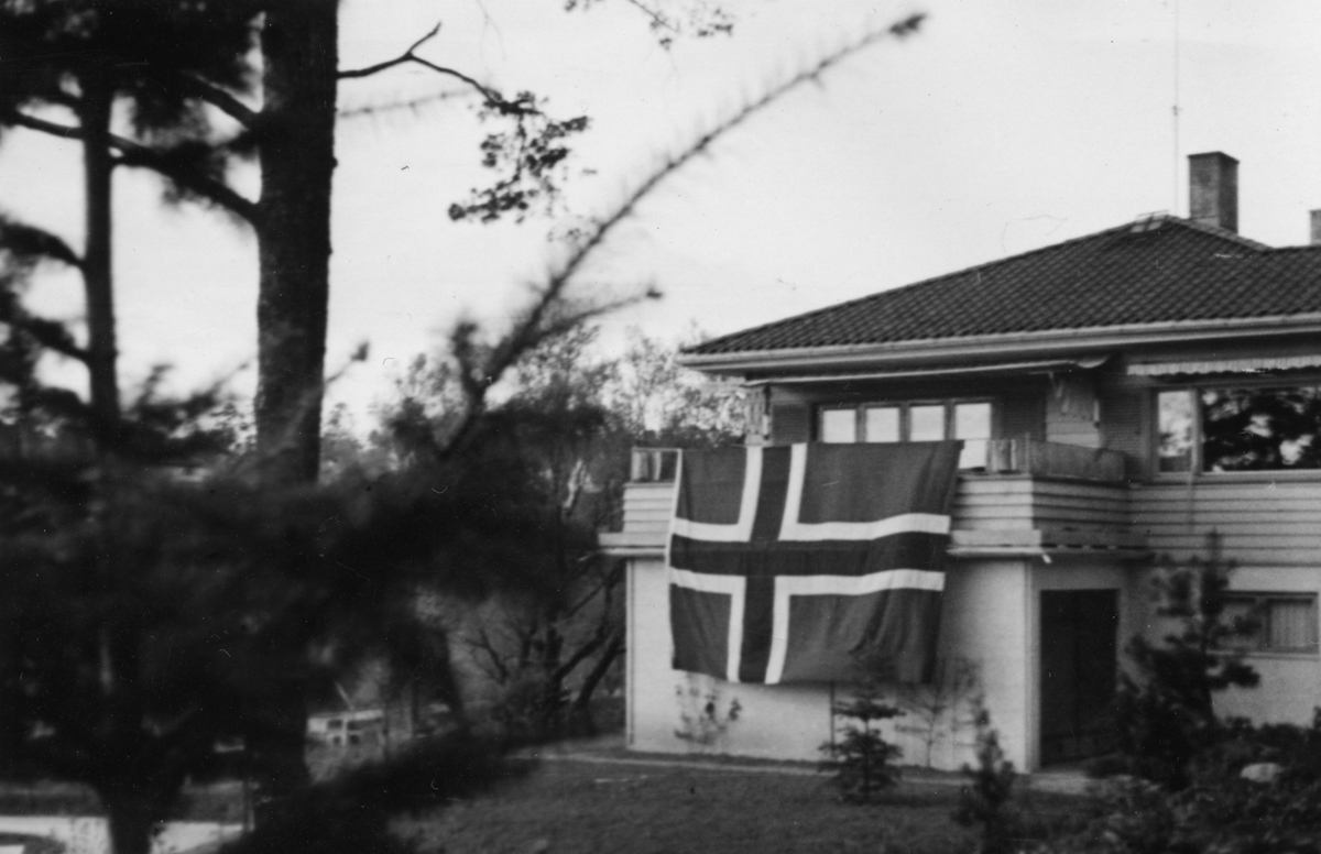 Stort, norsk flagg henger over balkongkanten på Ove og Ruth Hannestad sitt bolighus i Wergelandsvei 2.