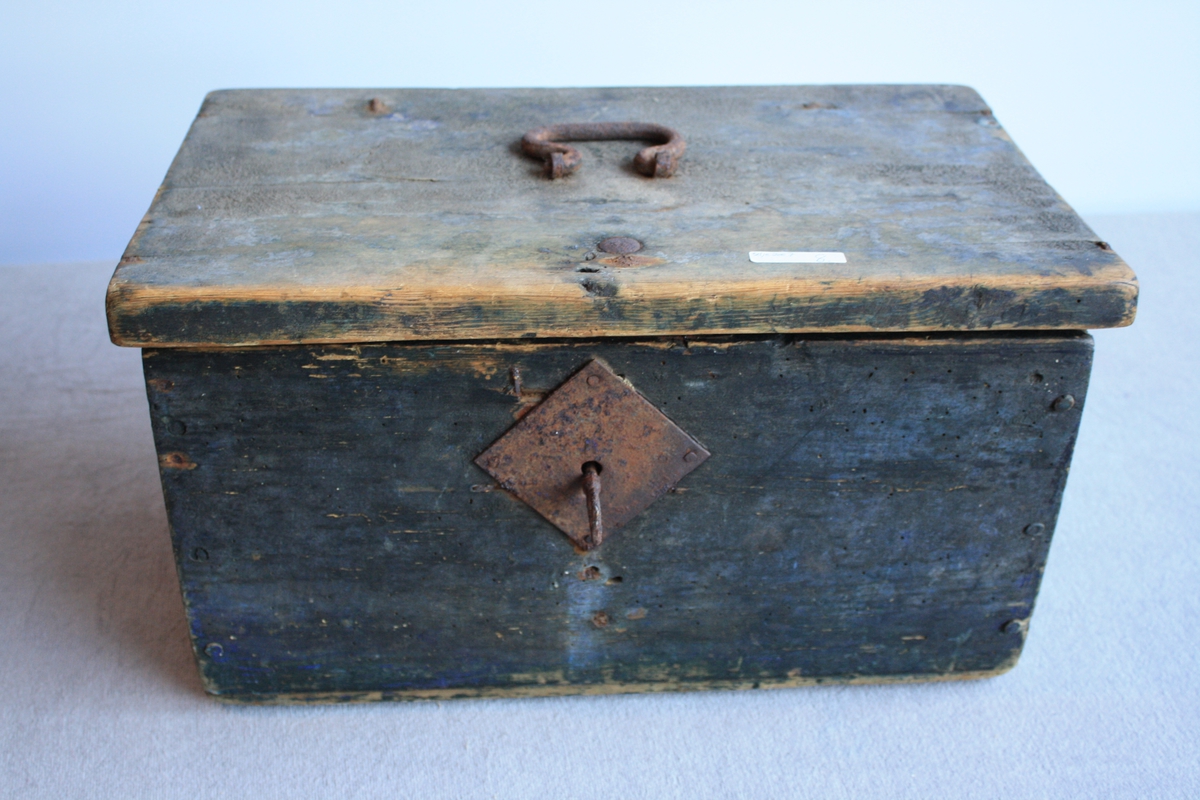 Svartmålt kiste med flatt lok. Metallhank på lok. Kista er set saman av trenaglar. Nøkkel står i lås.