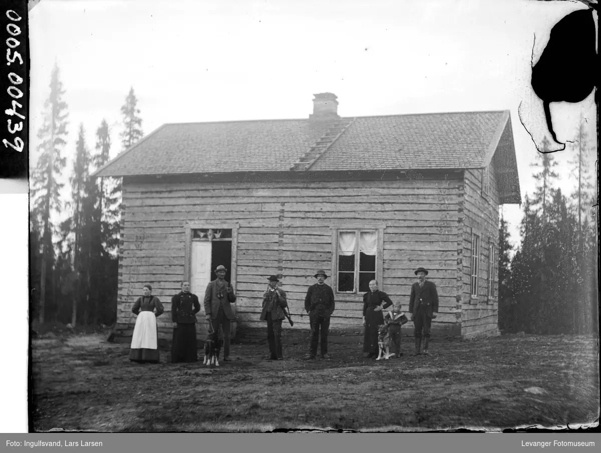 En gruppe mennesker foran et lafta bolighus.