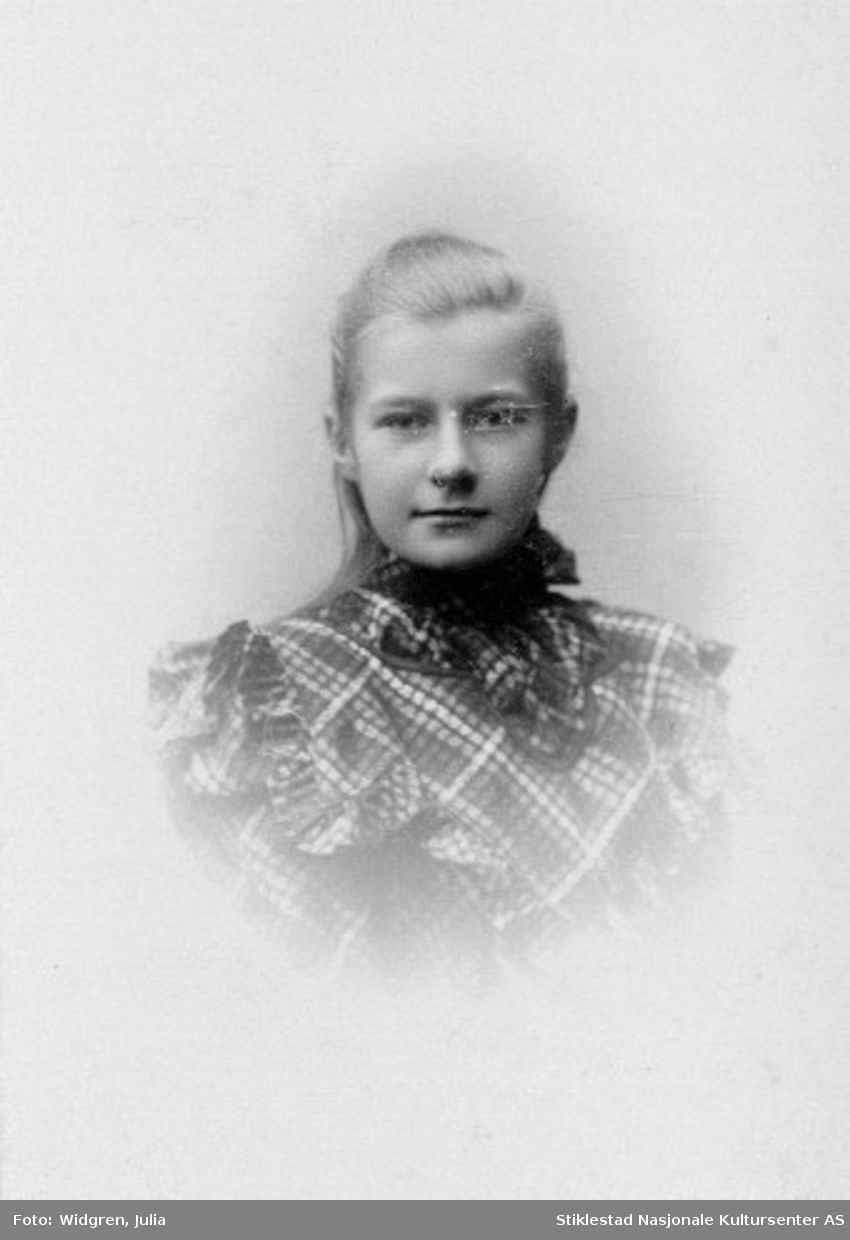 Portrett av Gunhilde Moe i kjole med ruter, rysjer og høy krage.
