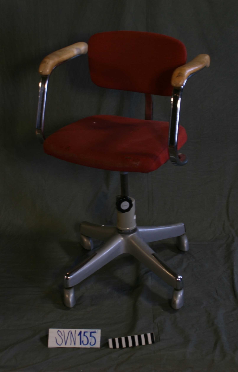 Regulerbar kontorstol med 4 hjul. Rødlig stofftrukket sete og -rygg. Armlener i metall og tre.
