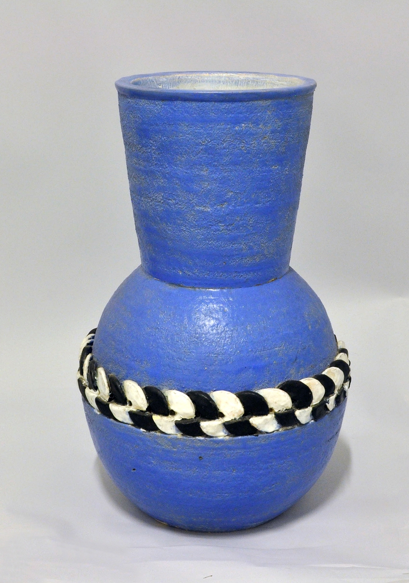 Stor vase av "keramikk". Tilnærmet kuleform med høy, vid hals. På midten et bånd av sirkulære plater som er kjedet i hverandre, med vekselvis sort og hvit glasur. Vasen har en ru overflate og er malt med blå farge. Form: Nora Gulbrandsen.