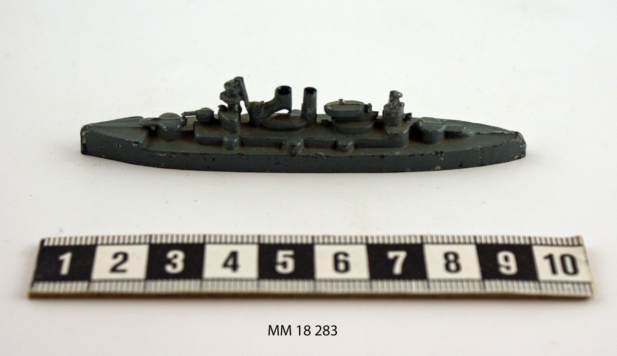 Fartygsmodell i form av pansarskeppet Sverige gjuten av metall i ett stycke, målad i grått. Spetsig för och akter. Plan botten. Artilleripjäser i för och akter, två skorstenar, torn.
