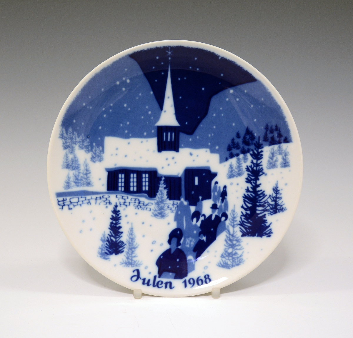 Juleplatte av porselen. Glatt modell. Hvit glasur. Dekorert med kirke og tekst Julen 1968 i ulike blåfarger.
Dekor av Gunnar Bratlie.