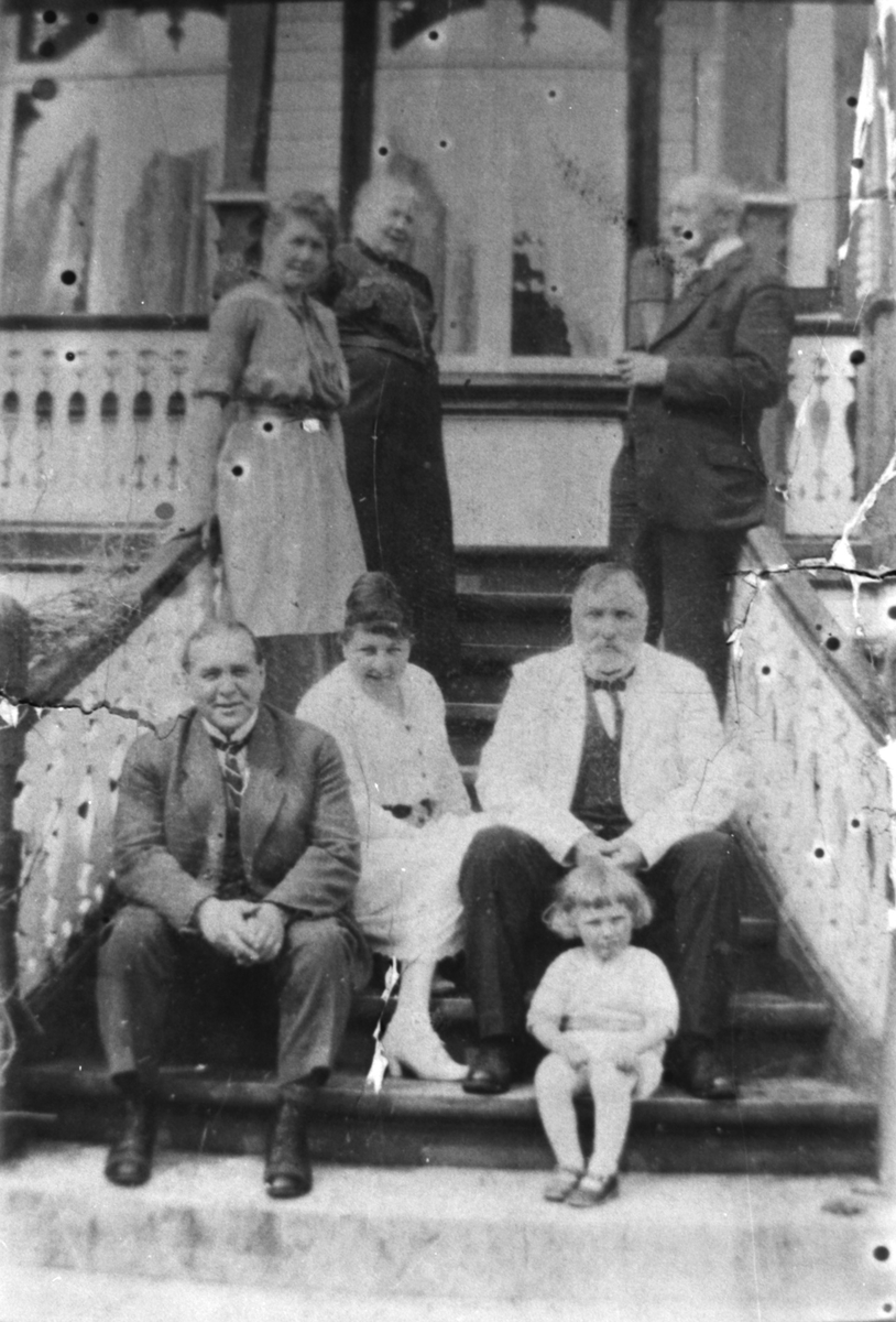 Sju personer på trappa foran Berlihuset. Mannen med skjegg identifisert som Børre Berli med kona Ellen til venstre.