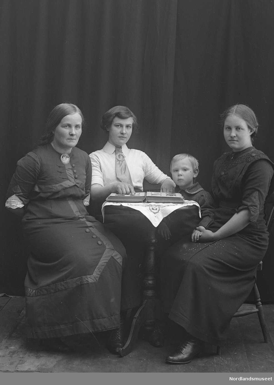 Portrett. 4 personer sitter sitter rundt et bord. Tre kvinner i 20-åra. En gutt ca. 7 år.