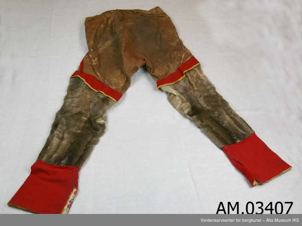 Pyntet med rødt og gult klede. Nederdelen av benet foret med samme bomullstoff som kragen på AM.03406 - Kofte. Velbrukt. Hull i buksebaken er lappet. 