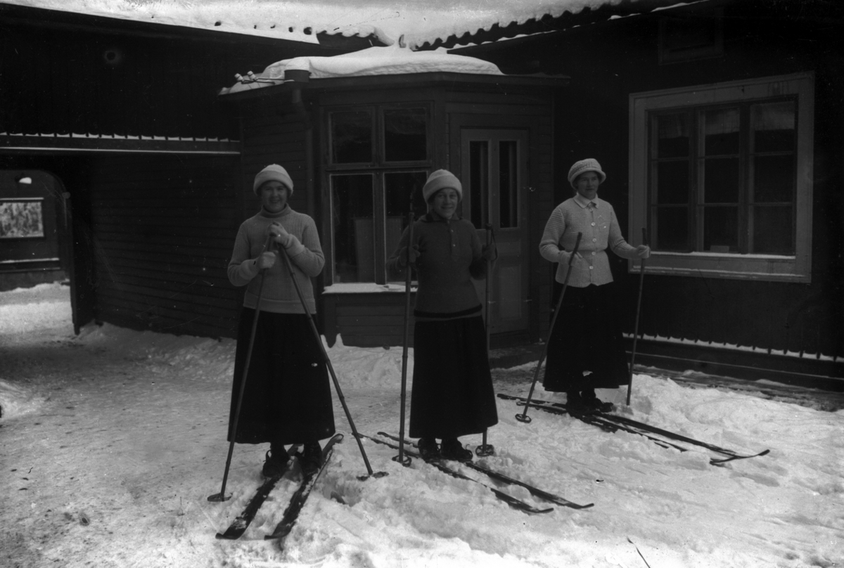 Tre unga kvinnor på skidor. I mitten Ester Pettersson (givarens faster).
I bakgrunden skrädderiet.