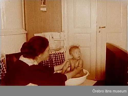 Rumsinteriör, en kvinna badar ett barn i baljan.
Gerda Thermaenius med dottern Maj.