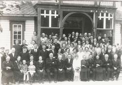 Gruppeportrett av et brudefølge på en trapp utenfor et hus.