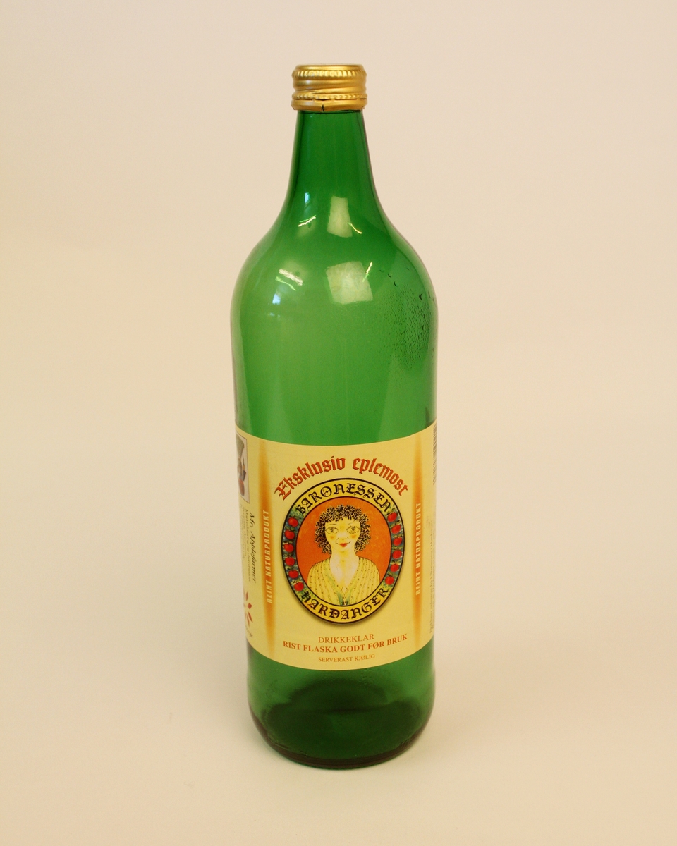 Flaske til eplemost med skrukork i metall. 1 liter. Flaska er brukt til "Eksklusiv eplemost" frå Baronessen av Hardanger. Det er litt uklart kva som er merkevarenamnet her. Flaska er grøn, og har éin etikett.