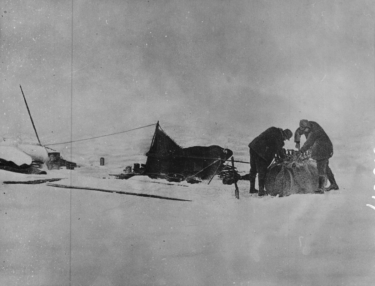 Lägret brytes. Till höger Andrée och Fraenkel vid den upp -och nedvända båten. Freankel var den starkast av de tre och han drog också den tyngsta bördan. Senare blev han på grund av fotbölden oförmögen att släpa sin kälke. Framtagning av bilderna gjordes av docent John Hertzberg år 1930 på Fotografi, Tekniska Högskolan.