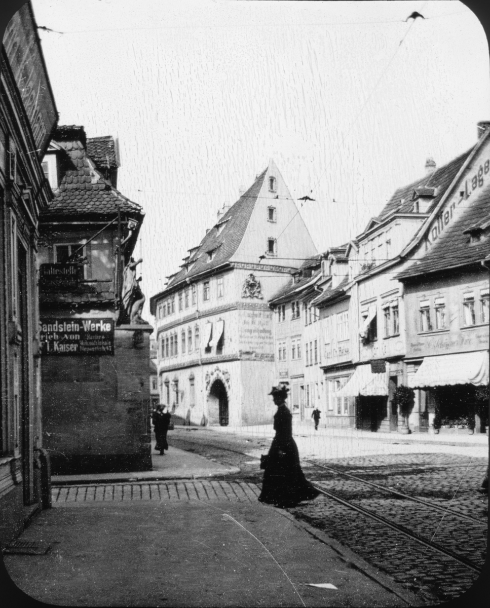 Skioptikonbild med motiv av kvinna som korsar rälsbelagd gata i Erfurt.
Bilden har förvarats i kartong märkt: Resan 1907. Erfurt 10. 14.