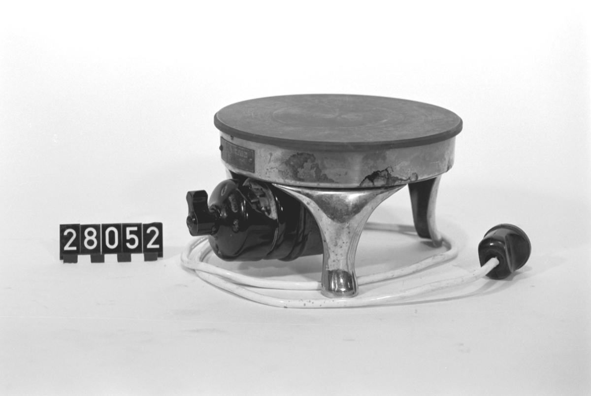 Elektrisk kokplatta, "Helios" 850 W, 220 V. Förnicklad trefot med trestegs strömställare (vridströmbrytare trasig) för 1/4, 1/2 och hel värmeeffekt.
Kat.Nr. 122528.