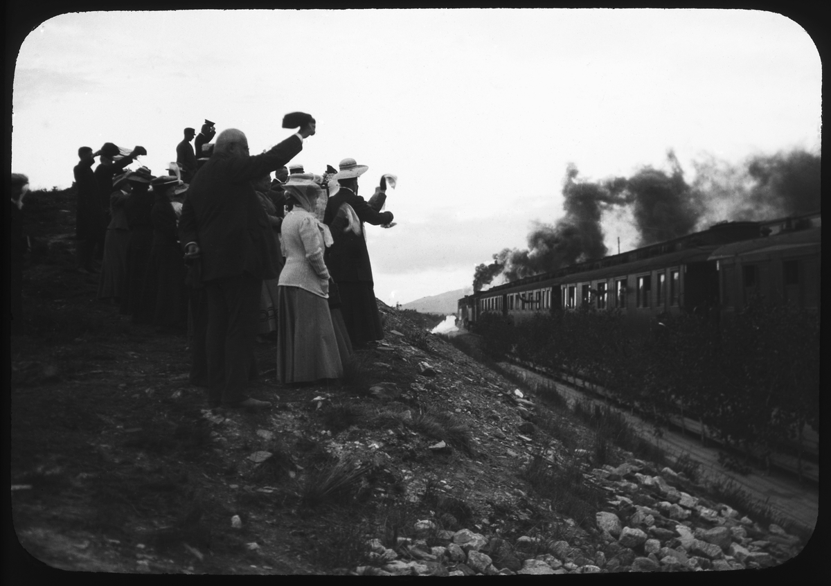 Kvinnor och män vinkar av resande vid ett tåg. Tåget med tre av SJs sovvagnar litt Ao1 först dras av dubbla ånglok.